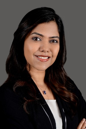 Image of the author, Nivedha Sridhar. A woman with dark black hair, black blazer, white shirt, smiling. 
